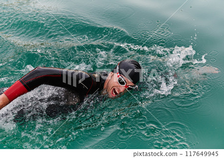A professional triathlete trains with unwavering dedication for an upcoming competition at a lake, emanating a sense of athleticism and profound commitment to excellence. A professional triathlete trains with unwavering dedication for an upcoming competition at a lake, emanating a sense of athleticism and profound commitment to excellence. 117649945