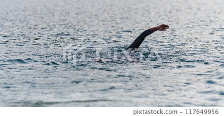 A professional triathlete trains with unwavering dedication for an upcoming competition at a lake, emanating a sense of athleticism and profound commitment to excellence. 117649956