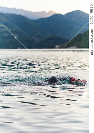A professional triathlete trains with unwavering dedication for an upcoming competition at a lake, emanating a sense of athleticism and profound commitment to excellence. 117649959
