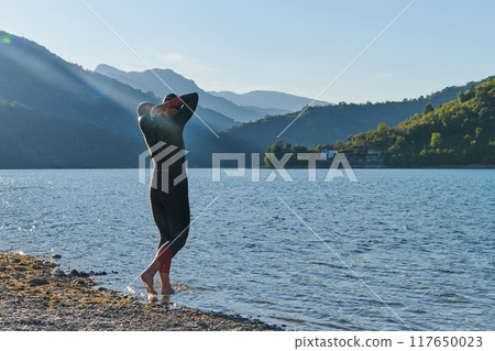 Authentic triathlon athlete getting ready for swimming training on lake Authentic triathlon athlete getting ready for swimming training on lake 117650023