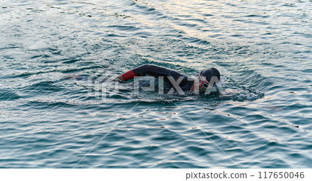 A professional triathlete trains with unwavering dedication for an upcoming competition at a lake, emanating a sense of athleticism and profound commitment to excellence. 117650046
