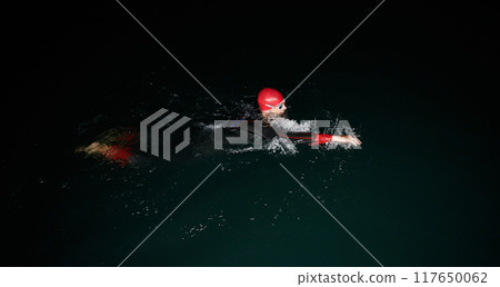 A determined professional triathlete undergoes rigorous night time training in cold waters, showcasing dedication and resilience in preparation for an upcoming triathlon swim competition 117650062