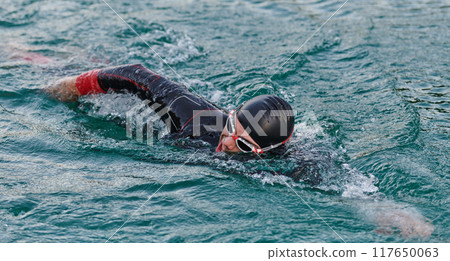 A professional triathlete trains with unwavering dedication for an upcoming competition at a lake, emanating a sense of athleticism and profound commitment to excellence. 117650063