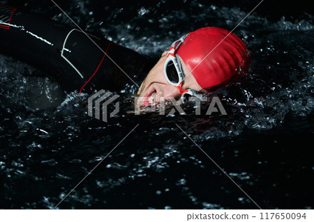 A determined professional triathlete undergoes rigorous night time training in cold waters, showcasing dedication and resilience in preparation for an upcoming triathlon swim competition 117650094