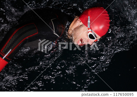 A determined professional triathlete undergoes rigorous night time training in cold waters, showcasing dedication and resilience in preparation for an upcoming triathlon swim competition 117650095