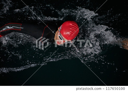 A determined professional triathlete undergoes rigorous night time training in cold waters, showcasing dedication and resilience in preparation for an upcoming triathlon swim competition 117650100