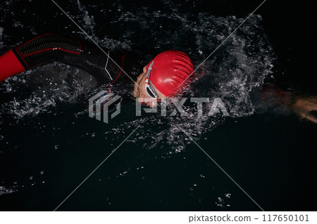 A determined professional triathlete undergoes rigorous night time training in cold waters, showcasing dedication and resilience in preparation for an upcoming triathlon swim competition 117650101