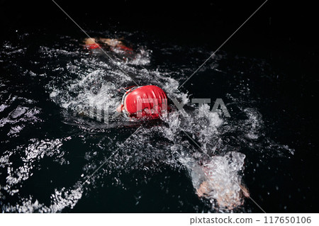A determined professional triathlete undergoes rigorous night time training in cold waters, showcasing dedication and resilience in preparation for an upcoming triathlon swim competition 117650106