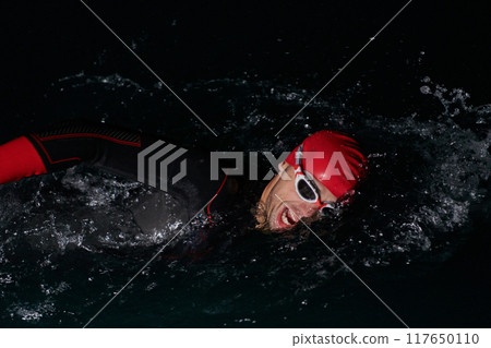 A determined professional triathlete undergoes rigorous night time training in cold waters, showcasing dedication and resilience in preparation for an upcoming triathlon swim competition 117650110