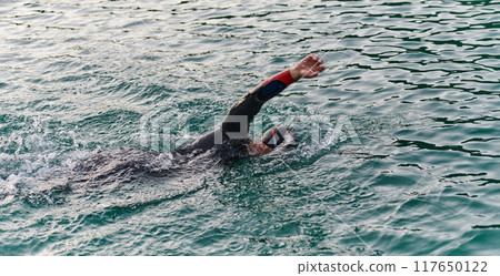 A professional triathlete trains with unwavering dedication for an upcoming competition at a lake, emanating a sense of athleticism and profound commitment to excellence. 117650122