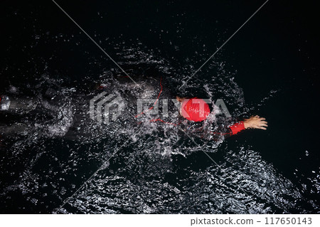 A determined professional triathlete undergoes rigorous night time training in cold waters, showcasing dedication and resilience in preparation for an upcoming triathlon swim competition 117650143