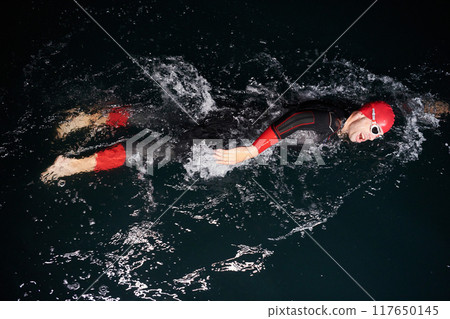 A determined professional triathlete undergoes rigorous night time training in cold waters, showcasing dedication and resilience in preparation for an upcoming triathlon swim competition 117650145