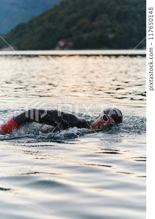 A professional triathlete trains with unwavering dedication for an upcoming competition at a lake, emanating a sense of athleticism and profound commitment to excellence. A professional triathlete trains with unwavering dedication for an upcoming competition at a lake, emanating a sense of athleticism and profound commitment to excellence. 117650148