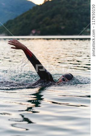 A professional triathlete trains with unwavering dedication for an upcoming competition at a lake, emanating a sense of athleticism and profound commitment to excellence. 117650150