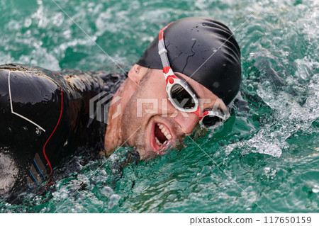 A professional triathlete trains with unwavering dedication for an upcoming competition at a lake, emanating a sense of athleticism and profound commitment to excellence. 117650159