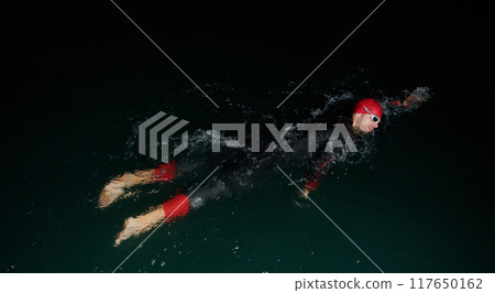 A determined professional triathlete undergoes rigorous night time training in cold waters, showcasing dedication and resilience in preparation for an upcoming triathlon swim competition 117650162