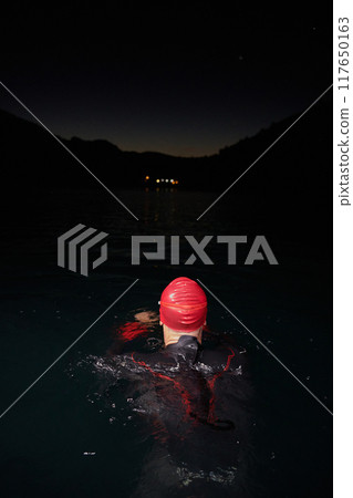 A determined professional triathlete undergoes rigorous night time training in cold waters, showcasing dedication and resilience in preparation for an upcoming triathlon swim competition 117650163