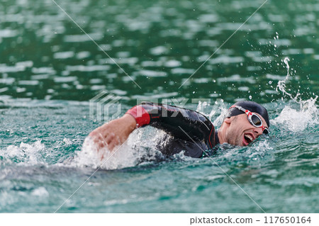 A professional triathlete trains with unwavering dedication for an upcoming competition at a lake, emanating a sense of athleticism and profound commitment to excellence. A professional triathlete trains with unwavering dedication for an upcoming competition at a lake, emanating a sense of athleticism and profound commitment to excellence. 117650164