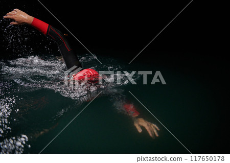 A determined professional triathlete undergoes rigorous night time training in cold waters, showcasing dedication and resilience in preparation for an upcoming triathlon swim competition 117650178