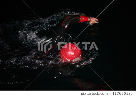 A determined professional triathlete undergoes rigorous night time training in cold waters, showcasing dedication and resilience in preparation for an upcoming triathlon swim competition 117650183