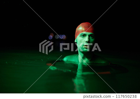 Authentic triathlete swimmer having a break during hard training on night neon gel light 117650238