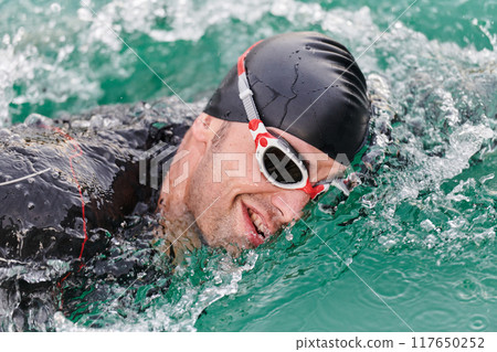 A professional triathlete trains with unwavering dedication for an upcoming competition at a lake, emanating a sense of athleticism and profound commitment to excellence. 117650252