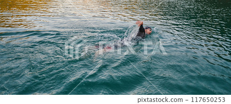 A professional triathlete trains with unwavering dedication for an upcoming competition at a lake, emanating a sense of athleticism and profound commitment to excellence. 117650253