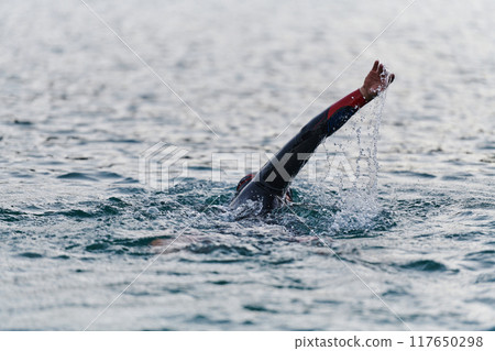 A professional triathlete trains with unwavering dedication for an upcoming competition at a lake, emanating a sense of athleticism and profound commitment to excellence. 117650298