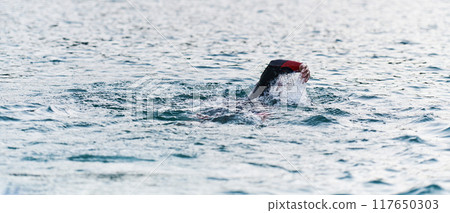 A professional triathlete trains with unwavering dedication for an upcoming competition at a lake, emanating a sense of athleticism and profound commitment to excellence. 117650303