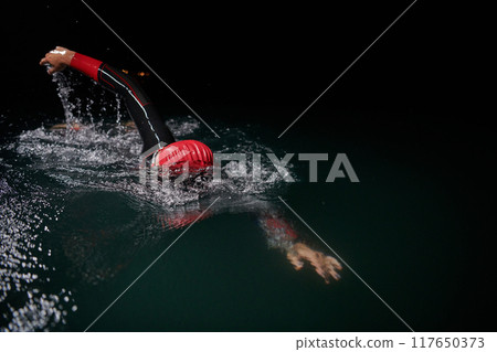 A determined professional triathlete undergoes rigorous night time training in cold waters, showcasing dedication and resilience in preparation for an upcoming triathlon swim competition 117650373