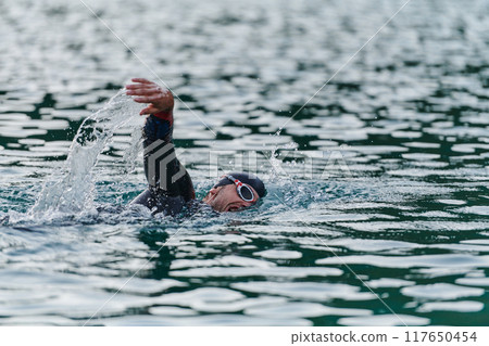 A professional triathlete trains with unwavering dedication for an upcoming competition at a lake, emanating a sense of athleticism and profound commitment to excellence. 117650454