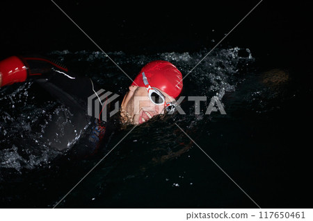 A determined professional triathlete undergoes rigorous night time training in cold waters, showcasing dedication and resilience in preparation for an upcoming triathlon swim competition 117650461