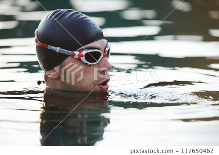 A triathlete finds serene rejuvenation in a lake, basking in the tranquility of the water after an intense training session 117650462
