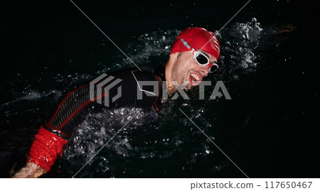 A determined professional triathlete undergoes rigorous night time training in cold waters, showcasing dedication and resilience in preparation for an upcoming triathlon swim competition A determined professional triathlete undergoes rigorous night time training in cold waters, showcasing dedication and resilience in preparation for an upcoming triathlon swim competition 117650467