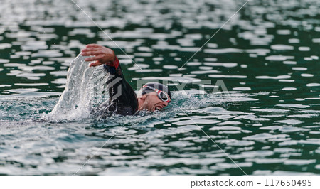 A professional triathlete trains with unwavering dedication for an upcoming competition at a lake, emanating a sense of athleticism and profound commitment to excellence. A professional triathlete trains with unwavering dedication for an upcoming competition at a lake, emanating a sense of athleticism and profound commitment to excellence. 117650495