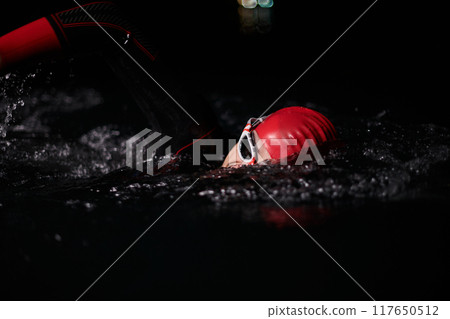 A determined professional triathlete undergoes rigorous night time training in cold waters, showcasing dedication and resilience in preparation for an upcoming triathlon swim competition 117650512