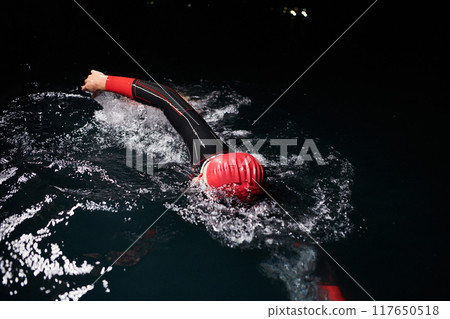 A determined professional triathlete undergoes rigorous night time training in cold waters, showcasing dedication and resilience in preparation for an upcoming triathlon swim competition 117650518