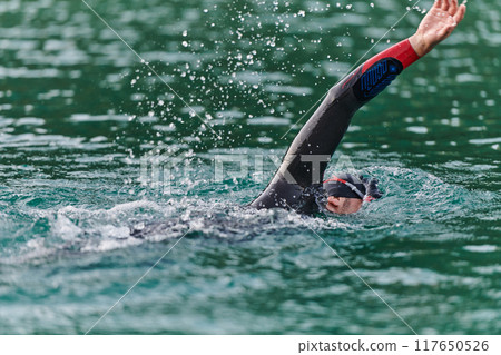 A professional triathlete trains with unwavering dedication for an upcoming competition at a lake, emanating a sense of athleticism and profound commitment to excellence. 117650526