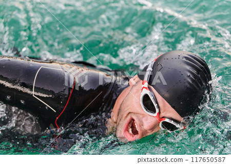 A professional triathlete trains with unwavering dedication for an upcoming competition at a lake, emanating a sense of athleticism and profound commitment to excellence. 117650587