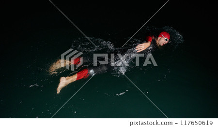 A determined professional triathlete undergoes rigorous night time training in cold waters, showcasing dedication and resilience in preparation for an upcoming triathlon swim competition A determined professional triathlete undergoes rigorous night time training in cold waters, showcasing dedication and resilience in preparation for an upcoming triathlon swim competition 117650619