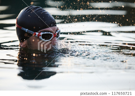 A triathlete finds serene rejuvenation in a lake, basking in the tranquility of the water after an intense training session 117650721