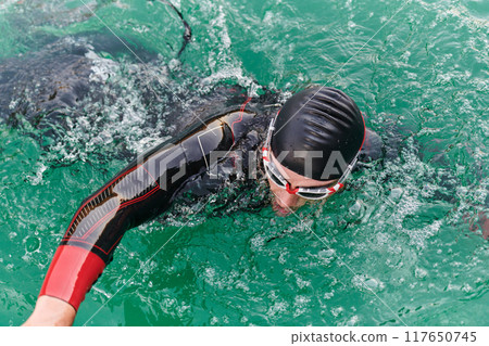 A professional triathlete trains with unwavering dedication for an upcoming competition at a lake, emanating a sense of athleticism and profound commitment to excellence. 117650745