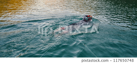A professional triathlete trains with unwavering dedication for an upcoming competition at a lake, emanating a sense of athleticism and profound commitment to excellence. 117650748
