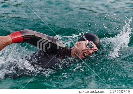 A professional triathlete trains with unwavering dedication for an upcoming competition at a lake, emanating a sense of athleticism and profound commitment to excellence. 117650749
