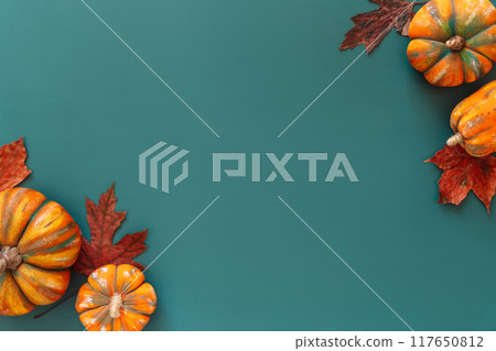 Artificial pumpkins with maple leaves lie in the corners of green background Artificial pumpkins with maple leaves lie in the corners of green background 117650812