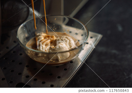 Coffee pouring from a coffee machine onto ice cream in a glass container 117650843