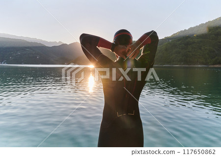 Authentic triathlon athlete getting ready for swimming training on lake Authentic triathlon athlete getting ready for swimming training on lake 117650862