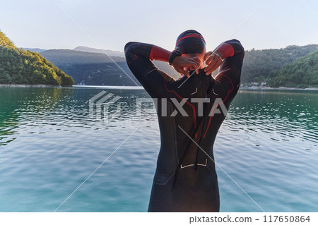 Authentic triathlon athlete getting ready for swimming training on lake Authentic triathlon athlete getting ready for swimming training on lake 117650864