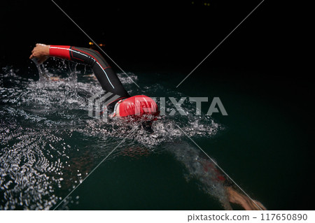 A determined professional triathlete undergoes rigorous night time training in cold waters, showcasing dedication and resilience in preparation for an upcoming triathlon swim competition 117650890