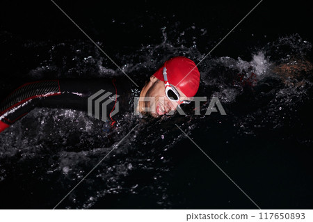 A determined professional triathlete undergoes rigorous night time training in cold waters, showcasing dedication and resilience in preparation for an upcoming triathlon swim competition 117650893